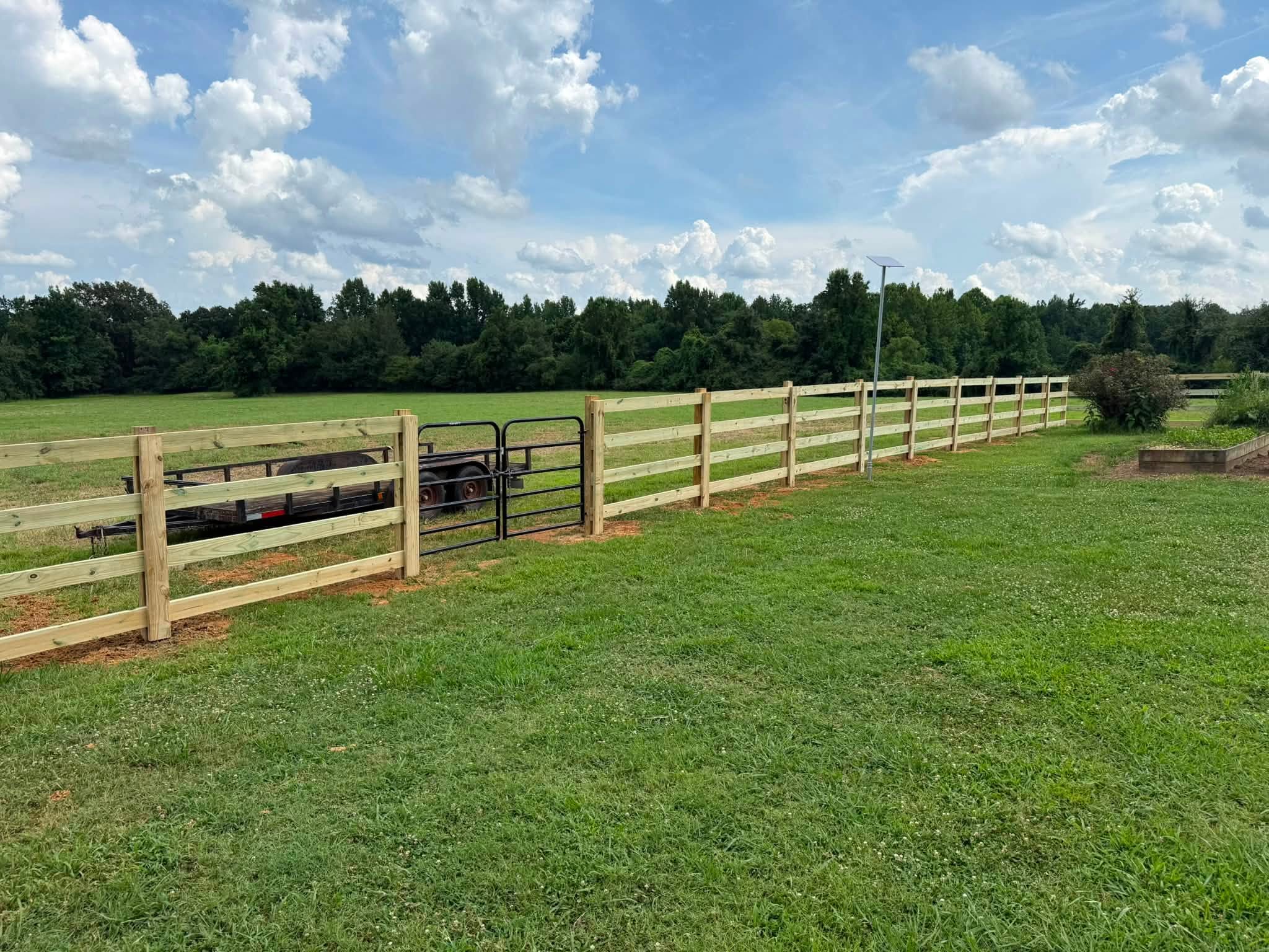Four-rail wood ranch fence with black metal gate in Northern Alabama