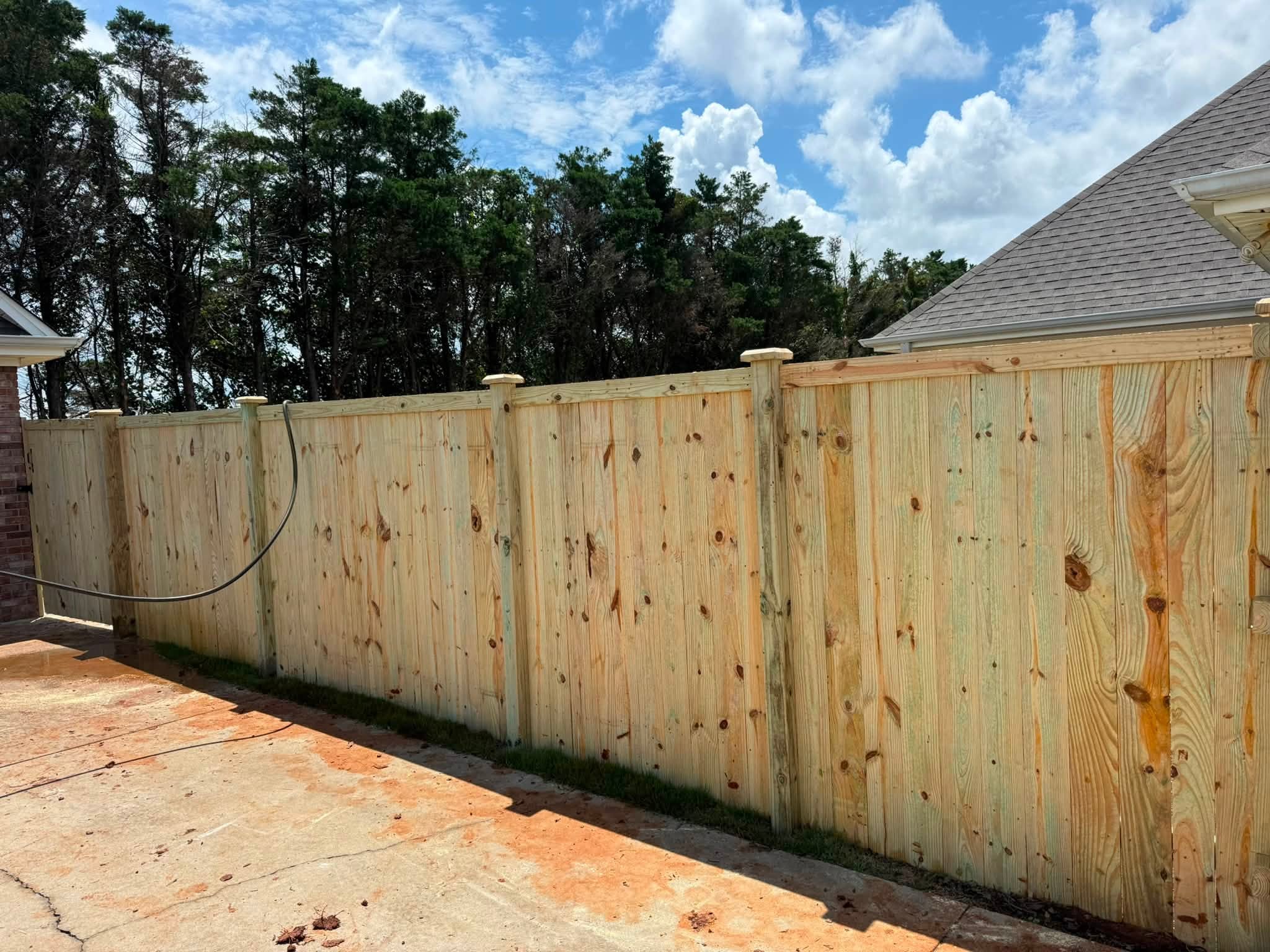 Fresh wood privacy fence installation along a driveway in Muscle Shoals, AL