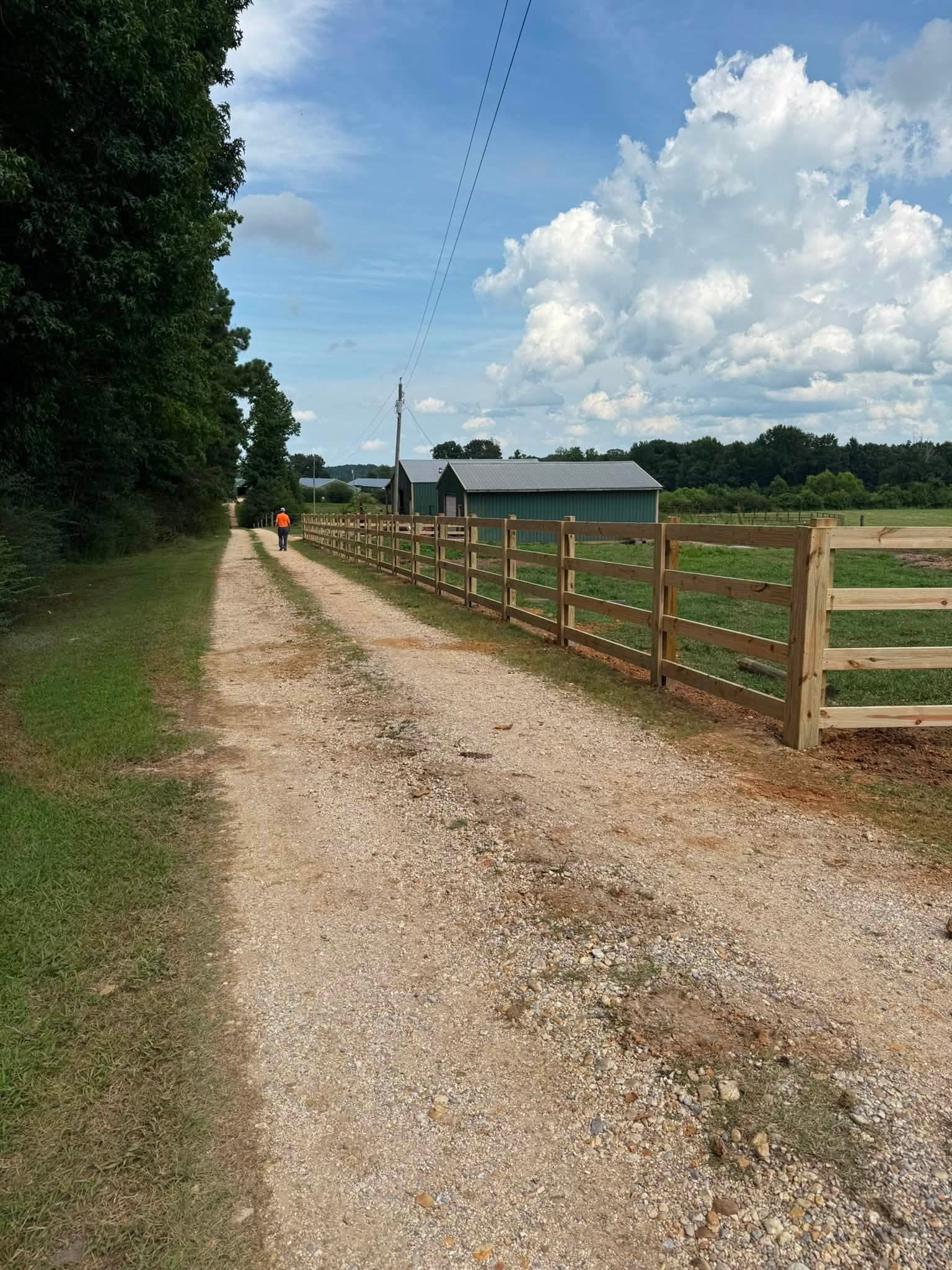 Four-rail wood farm fence along a gravel driveway in Northern Alabama