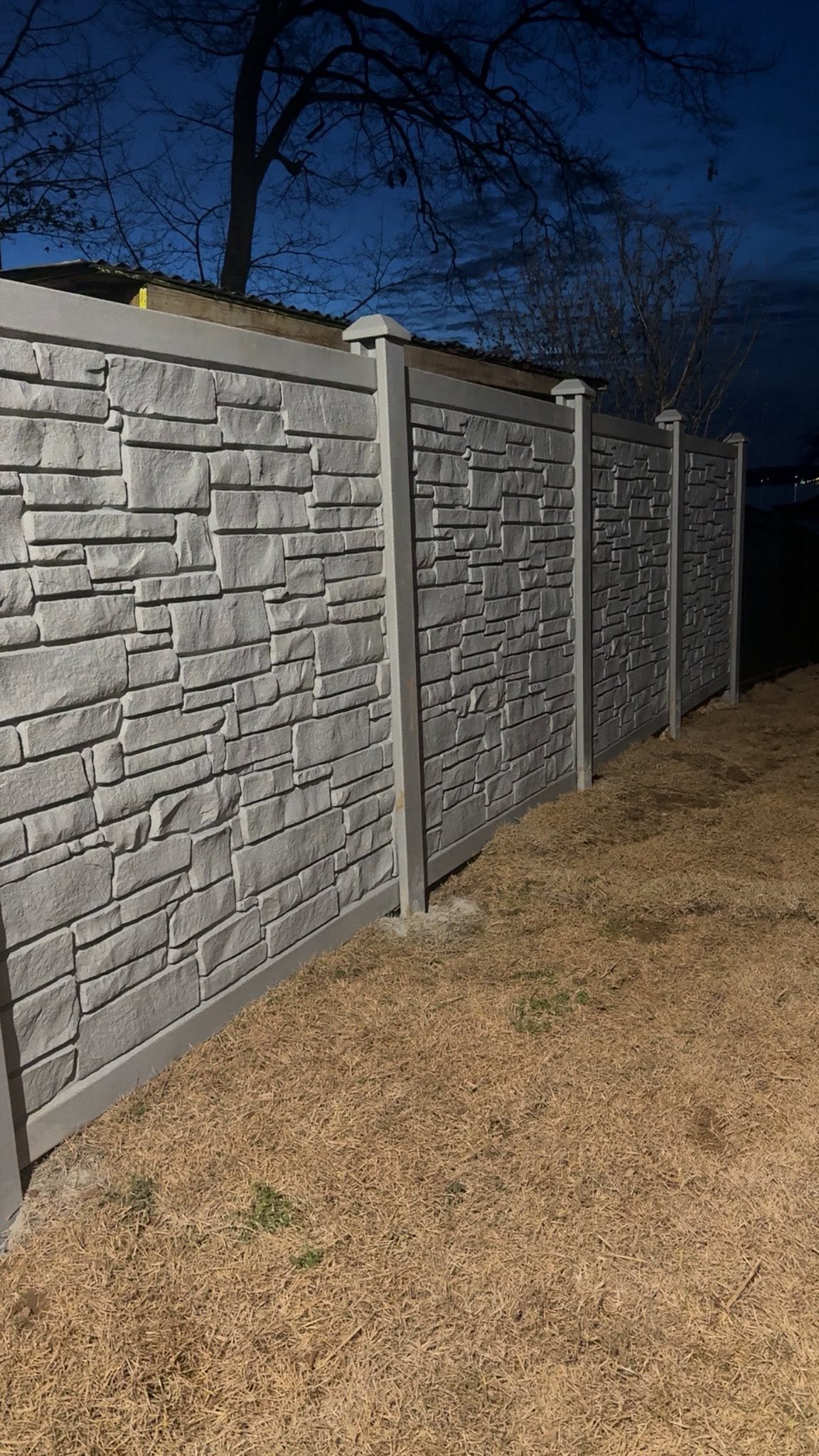 Stacked-stone textured privacy fence panels at dusk in Muscle Shoals, AL